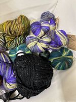 Group of variegated green-yellow, purple-cream, teal-green, and black skeins with reflective threads