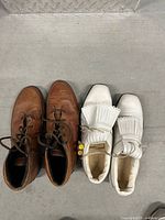 Brown LA Gear boots and white golf shoes side by side on floor