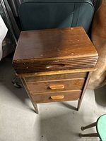 Front view of wooden sewing cabinet showing layered top and drawers