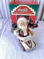 Santa figurine on scooter with Coca-Cola bottles, box in background