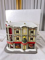 Front angled view of illuminated Jingles Department Store with snow roof and holiday decorations