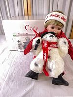 Cody doll seated with bear, box in background