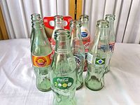Group of eight commemorative Coca-Cola bottles with carton in background