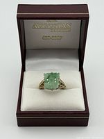 Ring front view in presentation box showing carved jade panel and gold gilt setting