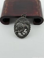 Front of sterling silver pendant showing mythical lion-dog design and scalloped edge