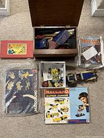 Overview of lot showing wooden box of parts, red Meccano box, magazines, black boxed set in plastic, Super Junior set, white box with model parts, assembled chassis