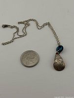Full necklace with pendant, bead and chain beside quarter for scale