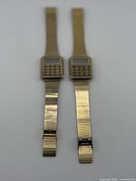 Front view of both gold-tone calculator watches showing LCDs and keypads