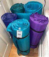 Five rolled camping mats standing upright, teal and purple colors, compression straps visible