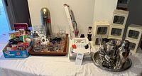 Overall lot on table showing shakers, trays, glasses, vacuum stoppers, boxed glassware