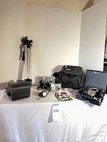 Overview of all items on table: Polaroid camera, two compact digital cameras, tripod, camera bag, accessories