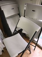 Stack of Lifetime plastic folding chairs folded and leaning against wall