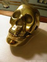 Front angled view showing skull face, teeth, eye and nose cavities, polished brass surface