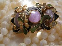 Front view of enameled clasp with amethyst cabochons surrounded by strands of mother of pearl beads