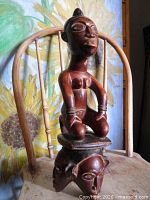 Full view of carved wood figure on triple-head base