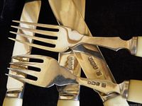 Close view of forks and knives showing sterling hallmarks and cream handles