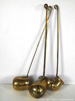 Front view of three brass ladles standing upright.