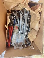 Top-down view into box showing combination wrenches, red pipe wrench and plastic case