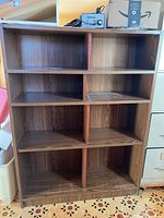 Front view of six-compartment brown wood-grain laminate bookcase showing shelves and divider