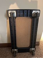 Underside of platform dolly showing black plastic frame, MDF center, four metal swivel casters