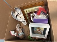 Top-down view of box showing carved angel wings, figurine, framed art, picture frame, metal stand, gift box and fabric