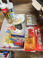 All items grouped in plastic tray: adhesive cartridges, filler tubes, wood glue bottle, epoxy pack, caulk plug set, honing oil tin