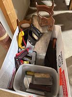 Box containing hand saws, trowels, sharpening stones, clamps, utility knife, bin