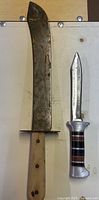 Front view of machete-style blade and hunting knife side by side
