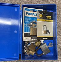 Overall view showing blue storage box containing two packaged padlocks, four loose padlocks and loose keys