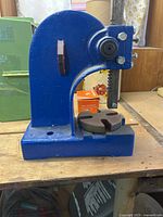 Front view of blue cast iron manual arbor press on bench