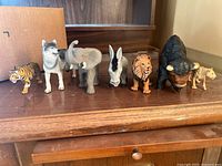 Front view of all seven plastic animal figurines lined on wooden surface