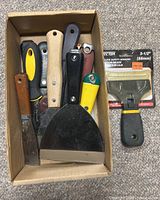 Box containing seven assorted putty knives and scrapers with varied handles plus one packaged Deflector Deluxe Safety Scraper