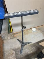 Full view of adjustable tripod roller support stand showing tripod base, vertical shaft, locking knob, and top bar with eight ball rollers