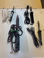Overview of five soldering irons laid out on table showing handles, tips, and cords