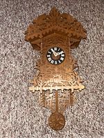 Full view of wooden scroll-saw cuckoo clock showing dial, cut-out design, and pendulum