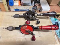 Both vintage hand drills side by side on workbench