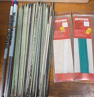All rods laid out: aluminum rods left, bundle of green-flux electrodes center, two sealed Spitfire packs right