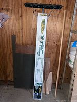 Boxed YardWorks roof rake leaning on wall