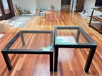 Both black metal frame tables with glass tops side by side