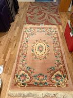 Both rugs laid out on floor showing size difference, pink floral in front, red leaf beyond