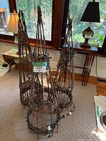 Three woven willow cone trellises standing together, two with string lights visible