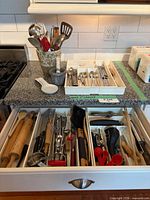 Drawer and countertop view showing majority of utensils, flatware tray, ceramic crock, spoon rest, mortar & pestle
