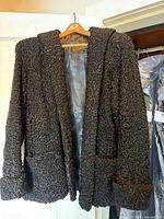 Full view of curly sheeps wool coat on hanger showing overall style, color, pockets and cuffs