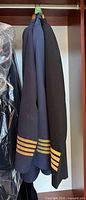 Two uniform jackets hanging, navy and black, both with gold sleeve braid visible