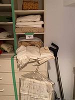 Shelving unit showing multiple folded linens, wicker sewing basket, garment bag