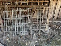 Group of rectangular metal tomato cages leaning against fence