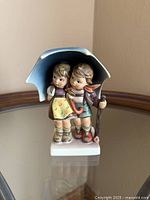 Front view of Hummel Stormy Weather figurine showing boy and girl under umbrella