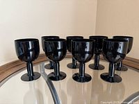 Eight black Noritake goblets on glass surface, angled front view