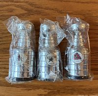 Front view of three silver mini Stanley Cup replicas in plastic wrap displaying Phoenix, Dallas and Columbus logos