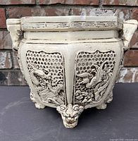 Front view of white ceramic planter with dragon and bird relief, footed base
